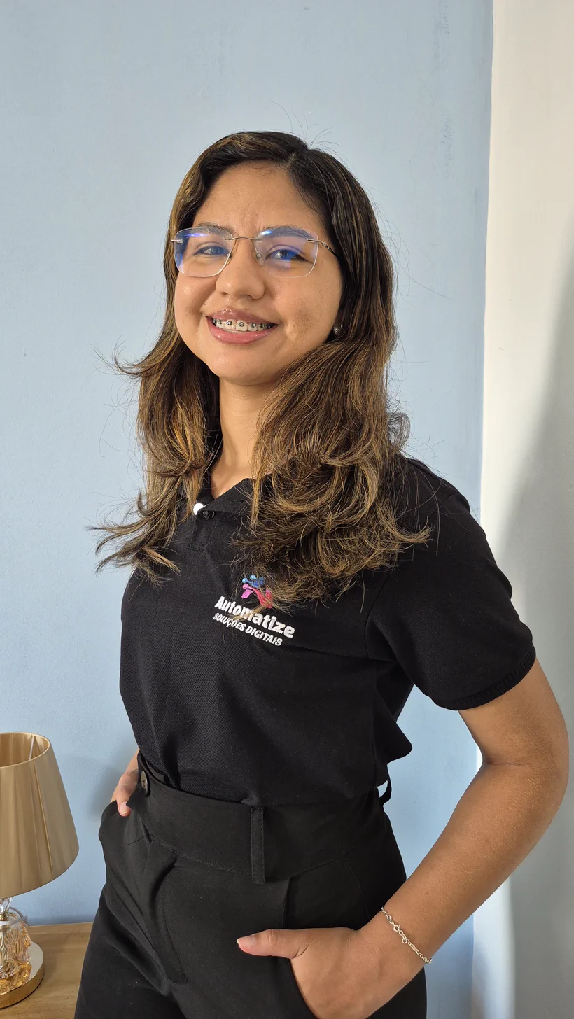 Lorena Marques, da Automatize, sorrindo com as mãos na cintura, de camisa polo preta bordada com o logotipo Automatize Soluções Digitais.